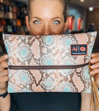 A happy woman holds up a Makeup Junkie Bag, which features an ingenious extended zipper to prevent contents from spilling. 